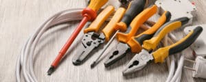 A Set Of Electrical Tools Including Pliers, Wire Strippers, A Screwdriver, And Cables On A Wooden Surface.
