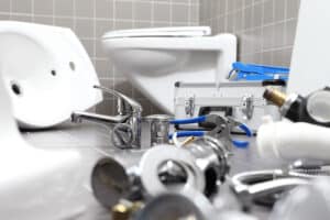 Plumbing Tools And Parts Scattered On A Bathroom Floor Near A Toilet, With A Tool Case In The Background.